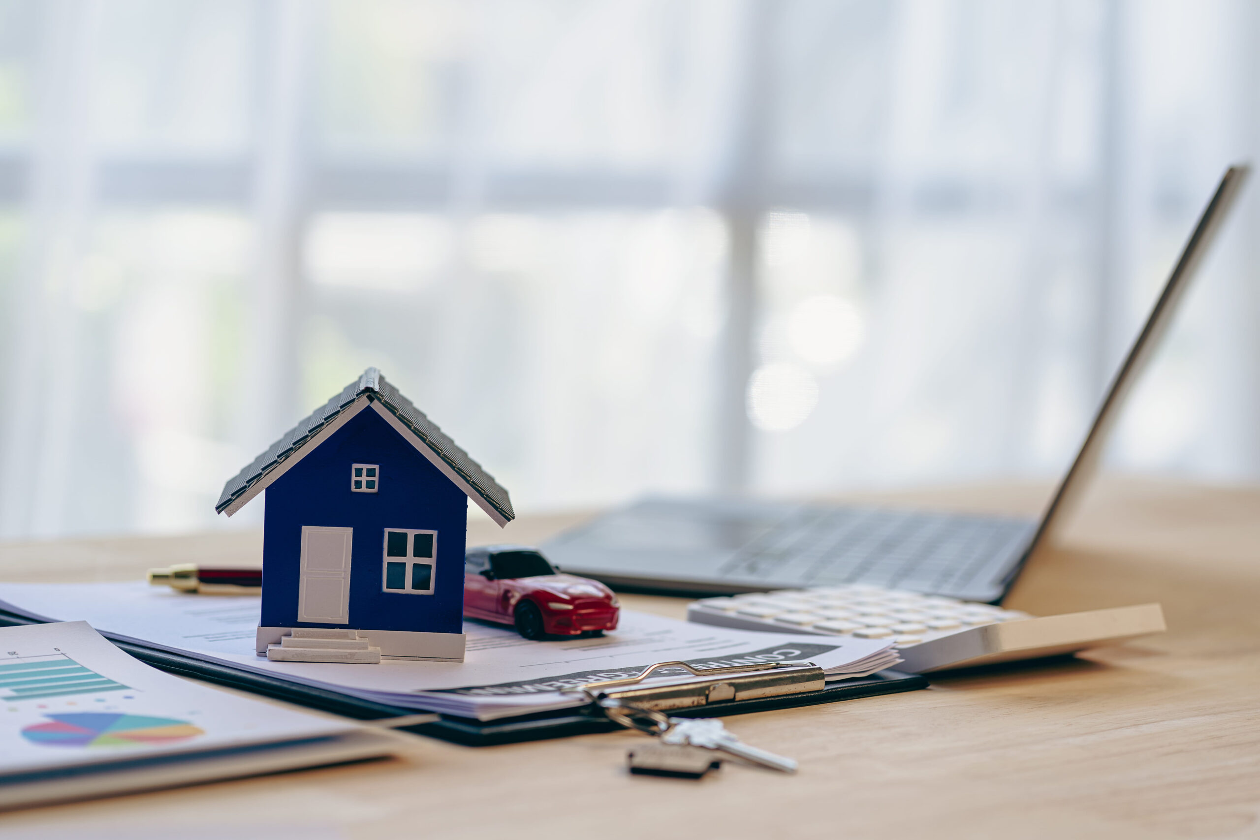 Blue model home, car, and keys on documents with laptop illustrating Dallas-Fort Worth real estate investments.